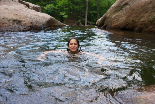 A person swims in a serene natural pool surrounded by rocks and lush greenery.
