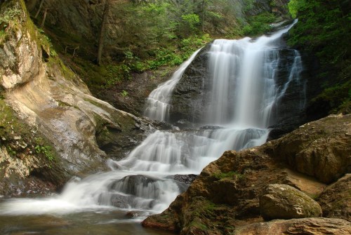 A serene waterfall cascading over rocky terrain, surrounded by lush greenery and natural rock formations.