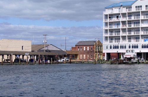 View of a waterfront with buildings, including a modern hotel and historic structures, under a cloudy sky.