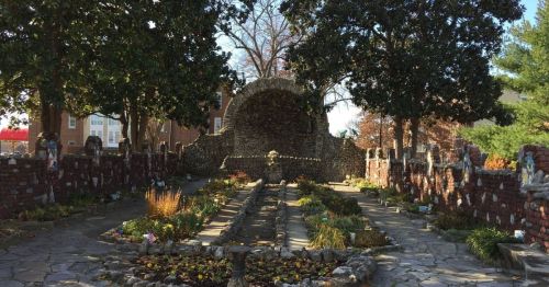 A serene garden with stone pathways, surrounded by trees and a stone archway, featuring colorful flowers and greenery.