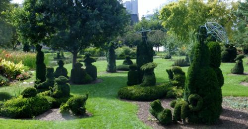 A lush garden featuring intricately shaped topiary sculptures among green grass and trees.