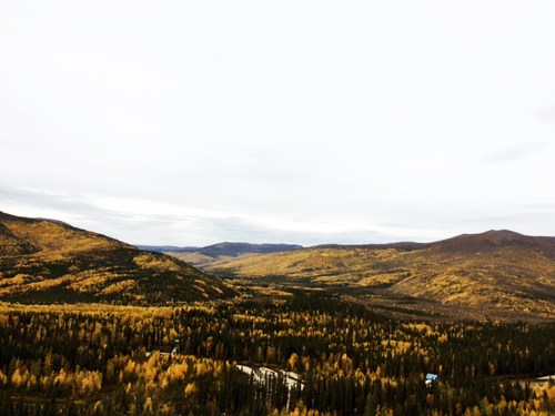 A panoramic view of rolling hills covered in autumn foliage, with a cloudy sky above.