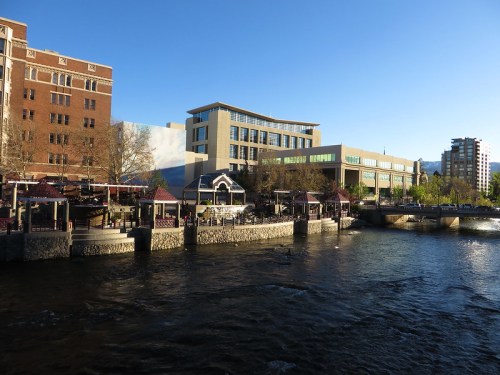 A riverside view featuring buildings, outdoor seating areas, and clear blue skies.
