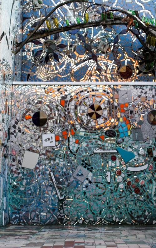 Colorful mosaic wall featuring various shapes and materials, reflecting light and creating intricate patterns.