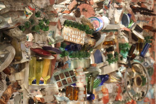 A colorful mosaic wall made of various glass bottles, tiles, and other materials, creating an artistic texture.