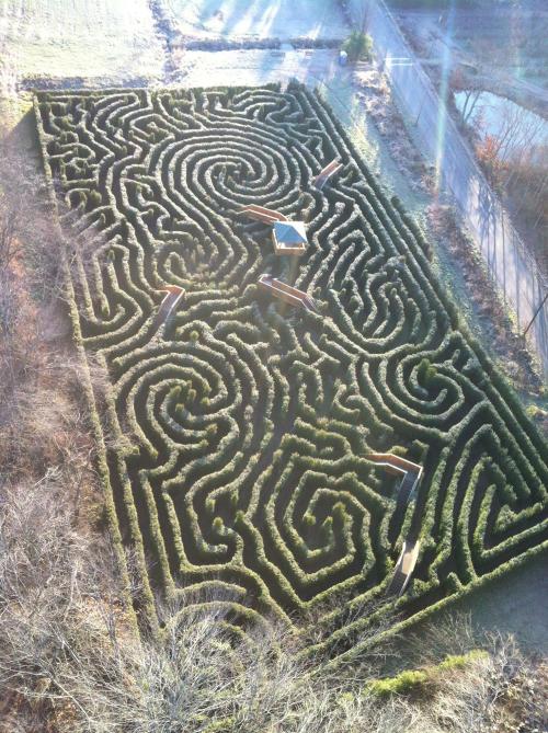 Aerial view of a large, intricate hedge maze with winding paths and a central gazebo.