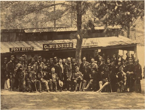 A historic group photo of soldiers and civilians outside a post office, with a sign reading "Col. Burnside."