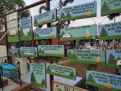 A display of colorful signs with humorous camping messages and illustrations of campers and nature.