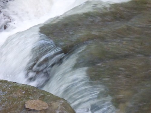 A close-up of flowing water over smooth rocks, creating a gentle cascade in a natural setting.