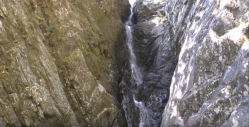 A narrow rocky gorge with a small waterfall cascading down the stones.