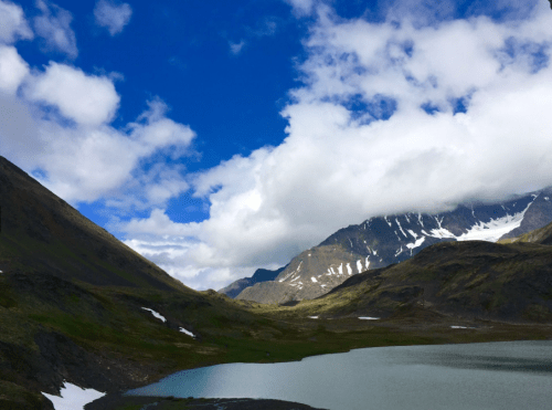 A serene landscape featuring mountains, a calm lake, and a blue sky with fluffy clouds.