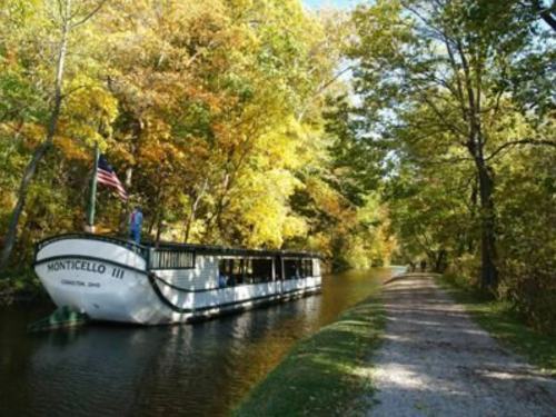 A canal boat named "Monticello III" docked beside a tree-lined path with vibrant autumn foliage.