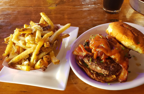 A plate with a juicy burger topped with sauce and bacon, alongside a serving of crispy fries.