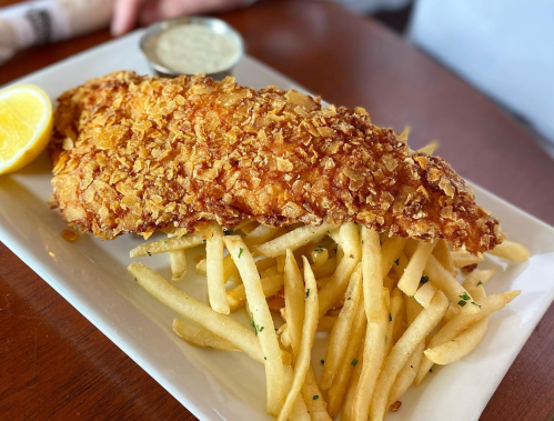 A plate of crispy fried fish fillet served with golden French fries and a lemon wedge.