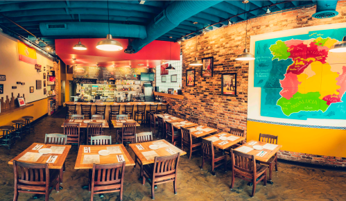 A vibrant restaurant interior with wooden tables, chairs, and a colorful map on the wall. Bar area in the background.