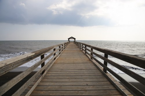 A wooden pier extends into the ocean under a cloudy sky, leading to a small gazebo at the end.