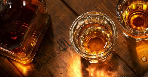 glass of whiskey next to a bottle of whiskey on a wooden table