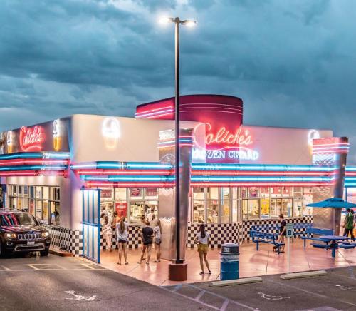 A vibrant ice cream shop with neon lights, people outside, and a cloudy sky in the background.