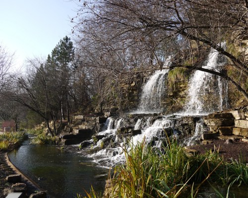 A serene waterfall cascading over rocks into a calm pond, surrounded by trees and greenery.