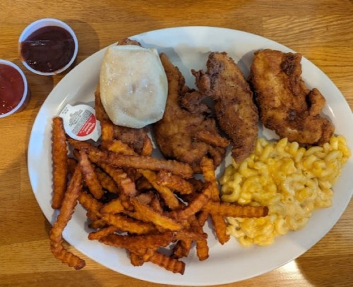 A plate of fried chicken, sweet potato fries, macaroni and cheese, a biscuit, and two cups of dipping sauce.