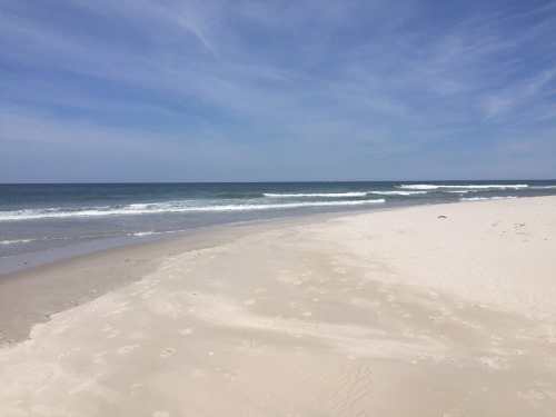 A serene beach scene with soft sand, gentle waves, and a clear blue sky.