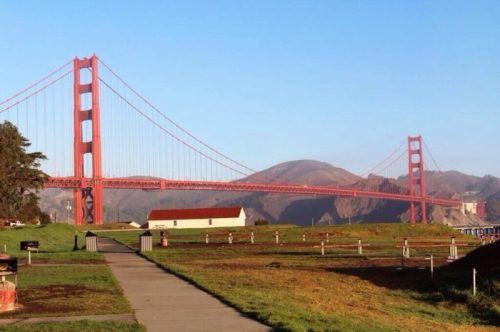 Golden Gate Bridge spanning a bay, with green grass and pathways in the foreground and hills in the background.