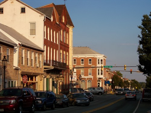 A quaint street scene featuring historic buildings, parked cars, and a traffic light under a clear blue sky.