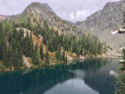 A serene mountain lake surrounded by lush green trees and rocky peaks under a cloudy sky.