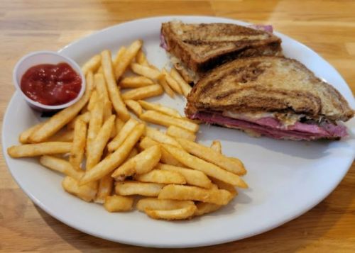 A plate with a grilled sandwich and a side of golden fries, accompanied by a small cup of ketchup.