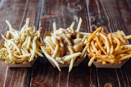 Three servings of French fries in paper trays: one with herbs, one topped with gravy, and one seasoned with spices.