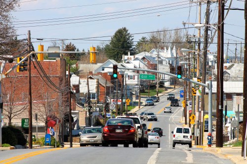 A view of a small town street with cars, traffic lights, and buildings lining the road under a clear sky.