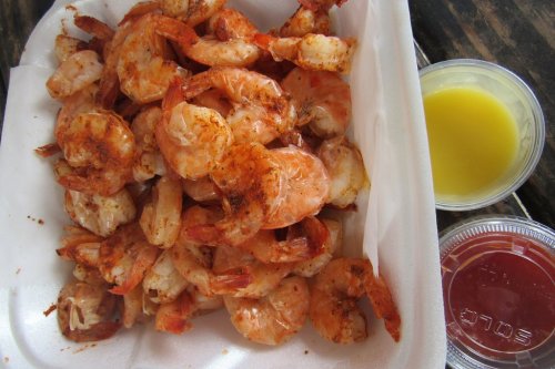 A container filled with seasoned shrimp, accompanied by lemon butter and cocktail sauce in small cups.