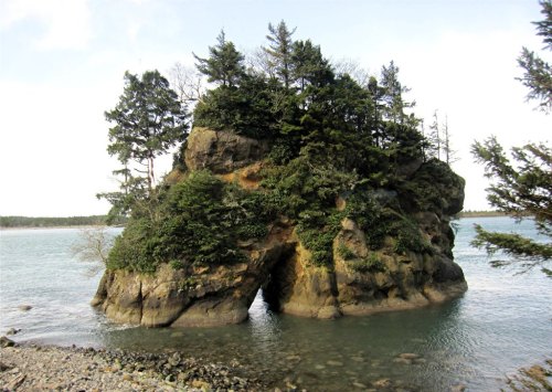 A rocky island with trees on top, surrounded by calm water and a cloudy sky.