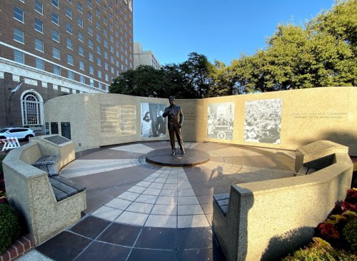 A statue of a man stands in a circular memorial with stone benches and historical photos on the walls.