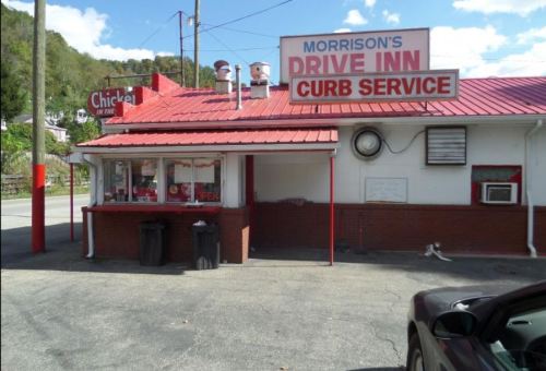 A small drive-in restaurant with a red roof and sign, featuring a curb service area and a window for orders.
