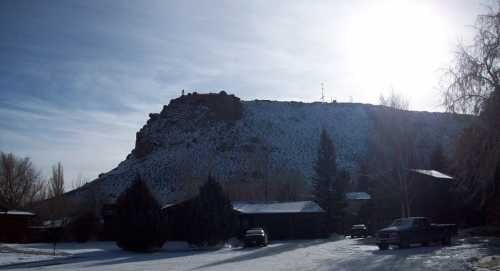 A snowy landscape with a rocky hill in the background, sunlight shining from the left, and parked vehicles in the foreground.