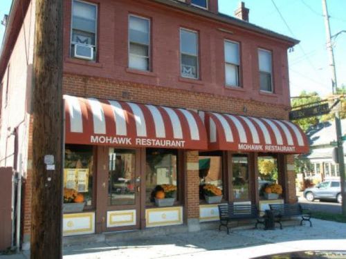 Exterior of Mohawk Restaurant featuring red and white striped awnings and flower pots by the windows.