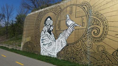 A mural depicting a person in a gas mask holding a pigeon against a gold background with intricate designs.