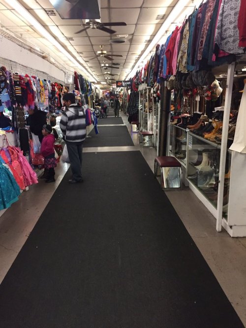 A busy indoor market aisle lined with clothing racks and shoppers browsing costumes and apparel.