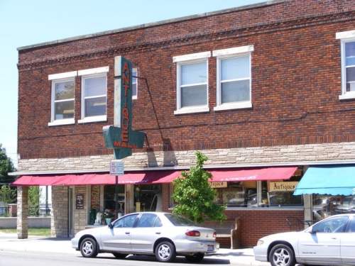 A brick building with an antique shop sign, featuring awnings and parked cars in front.