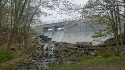 A concrete dam with water flowing over it, surrounded by trees and rocky terrain.