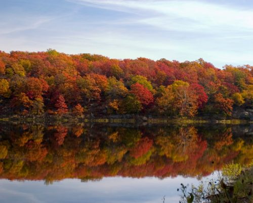 Vibrant autumn foliage reflects on a calm lake under a clear blue sky.