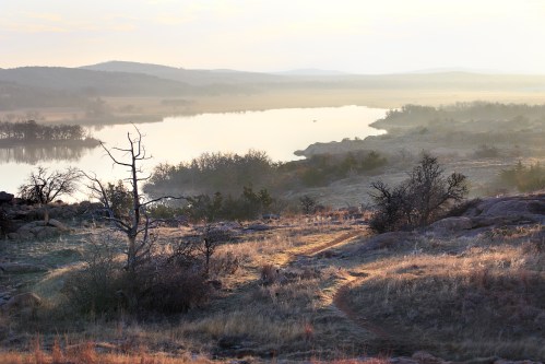 A serene landscape featuring a river, rolling hills, and a winding path through grassy terrain at sunrise.