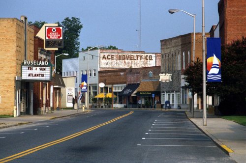 A quiet small-town street with storefronts, banners, and a clear sky, evoking a nostalgic atmosphere.