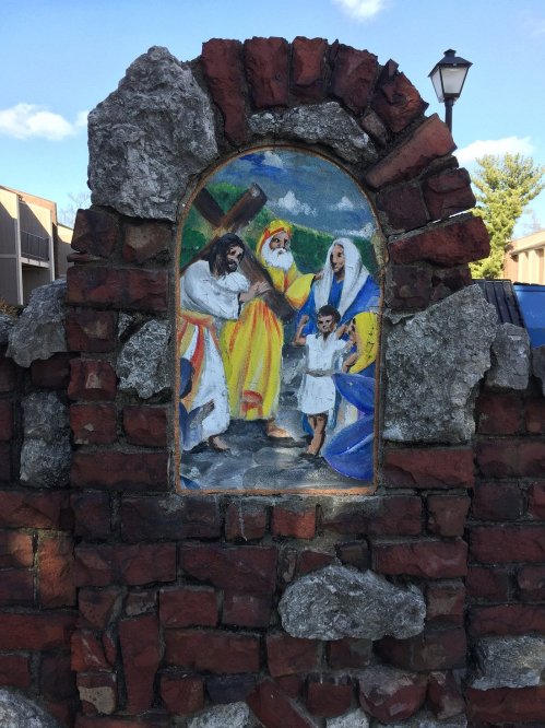 A colorful mural depicting a biblical scene, framed by a weathered brick wall with stones.
