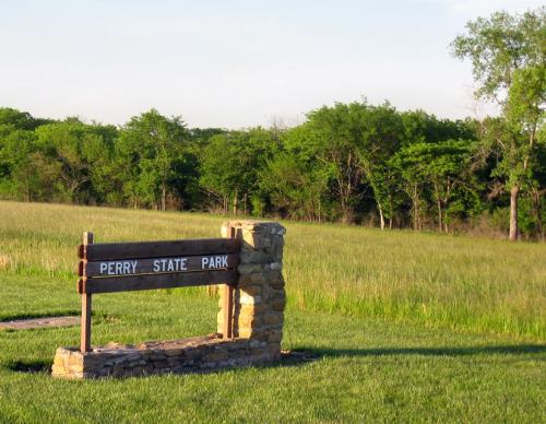 Sign for Perry State Park in a grassy area with trees in the background under a clear blue sky.