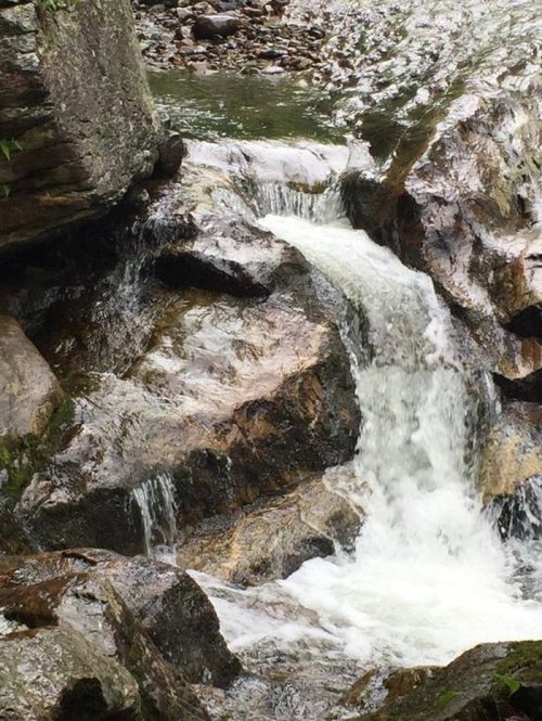 A serene waterfall cascading over rocky terrain, surrounded by lush greenery and flowing into a calm stream.
