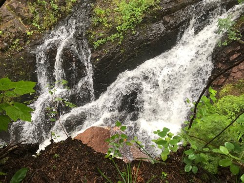 A cascading waterfall flows over rocky terrain, surrounded by lush green foliage.