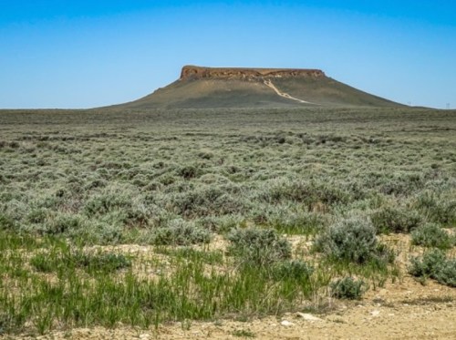 A flat-topped mesa rises above a vast, grassy plain under a clear blue sky.