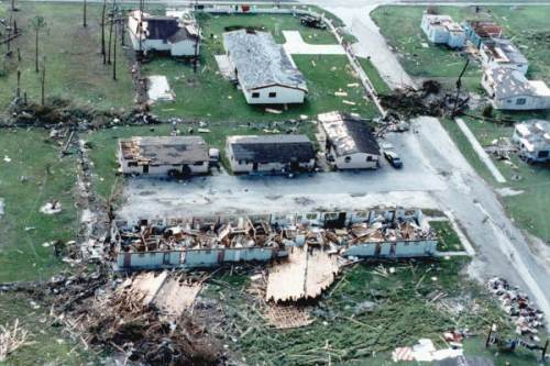Aerial view of a neighborhood showing extensive damage from a storm, with destroyed roofs and debris scattered around.